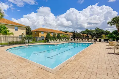 a large swimming pool with chairs and a building at 4 Mi to Disney! Family Townhome with Pool Access in Kissimmee