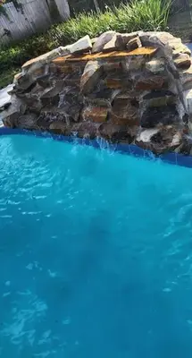 a swimming pool with a stone wall and blue water at Ava Lea's Falls in Orlando