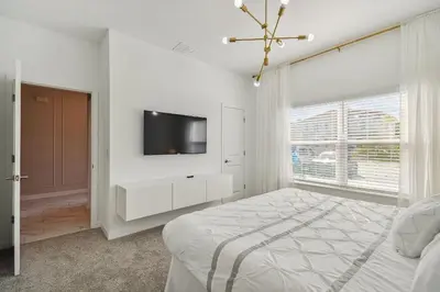 a white bedroom with a bed and a tv on a wall at Luxuosa Casa 4Q/3B Storey Lake in Kissimmee
