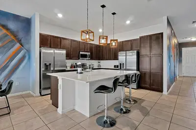 a kitchen with a large white island with bar stools at Luxury 12-BR Villa w/ Pool & Resort Amenities Near Disney in Kissimmee