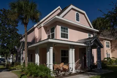 a pink house with a palm tree on a street at Magical Themed 3BR Townhouse Near the Parks in Kissimmee