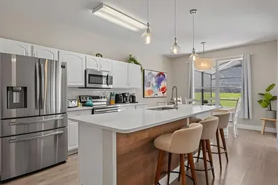 a kitchen with white cabinets and a large island with bar stools at Casa Luxo 4Q c/ Piscina e Game Room Avengers in Orlando