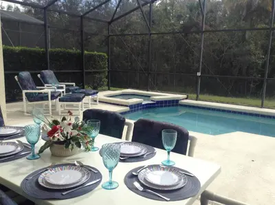a table with plates and wine glasses next to a pool at Grand Cumbrian - Four Bedroom Home in Kissimmee