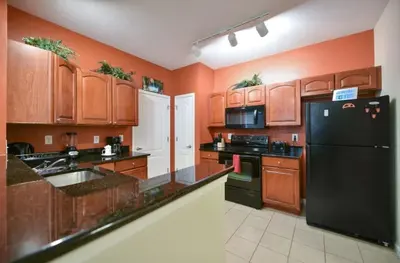 a kitchen with wooden cabinets and a black refrigerator at Resort Condo with all amenities needed-Cane Island in Kissimmee