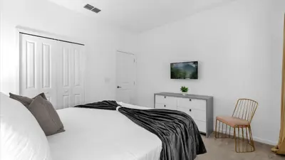 a white bedroom with a bed and a chair at Summer Getaway in FL - 6BR Home with Private Pool! in Kissimmee