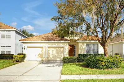 a white house with a garage and a tree at Personally Designed Home w/ Pool, Game Room near Disney in Orlando