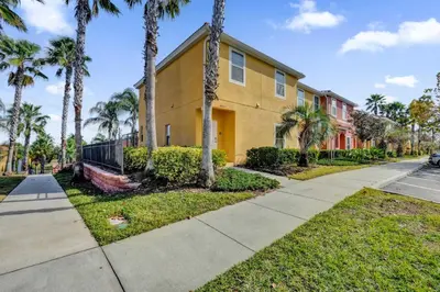 a yellow house with palm trees and a sidewalk at Upstay Spacious 3BR Home w Resort Access in Kissimmee