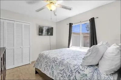 a bedroom with a bed with a ceiling fan and a window at Cozy Home Near Disney With Private Pool in Kissimmee