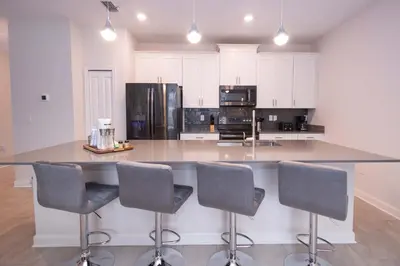 a kitchen with a large island with four bar chairs at 2901 SS Discover Opulence 4-Bedroom Villa with Pool, and Magical Themed Rooms! in Kissimmee