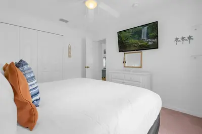 a white bedroom with a white bed and a flat screen tv at Upstay - Games & Private Pool Family Home in Orlando