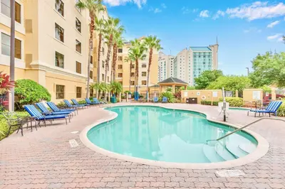 a swimming pool with chairs and palm trees and buildings at Suite with Pool and Hot Tub - Close to Near Disney in Orlando