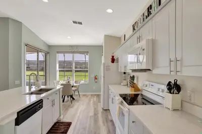 a kitchen with white cabinets and a dining room with a table at Luxury Pool Home 3 Miles from Disney & More! in Kissimmee