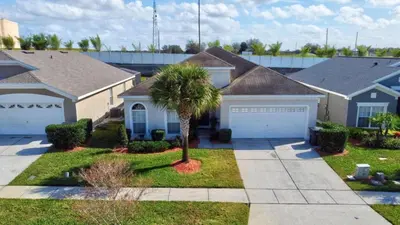a house with a palm tree in the front yard at Luxury Pool Home 3 Miles from Disney & More! in Kissimmee