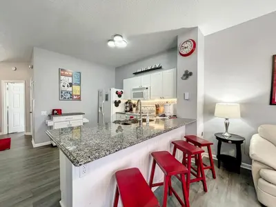 a kitchen and living room with a counter and red stools at Mickey's Play House: Family Fun & Comfort in Kissimmee