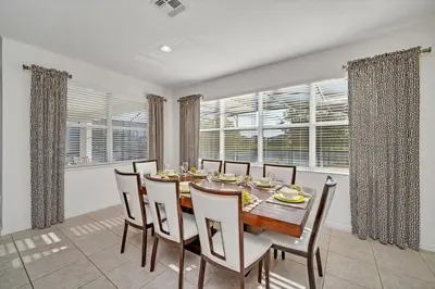 a dining room with a table and chairs and windows at DREAM VILLA 6bd, all en-suite, pool, spa, grill, theatre in Kissimmee