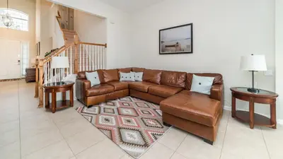 a living room with a brown leather couch and tables at Amazing 5 BR Home with Pool Windsor Hills Resorts in Orlando
