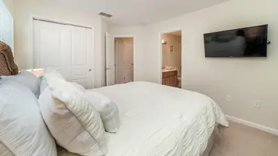 a bedroom with a white bed with a television on the wall at Amazing 5 BR Home with Pool Windsor Hills Resorts in Orlando