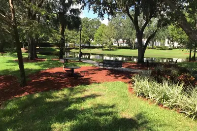 a park with benches and a pond and trees at Villa Port - Lucaya Village in Kissimmee