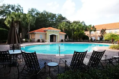a pool with chairs and an umbrella and a building at Villa Compass- Compass Bay in Kissimmee
