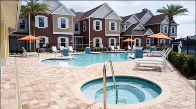 a swimming pool with chairs and umbrellas in front of houses at Disney here we go in Orlando
