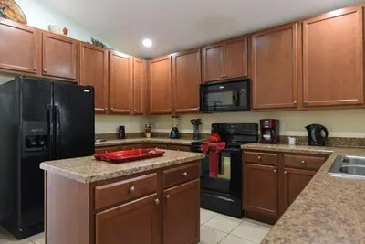 a kitchen with wooden cabinets and a black refrigerator at Veranda Palms Villa: Pool, Spa & Game Room in Kissimmee