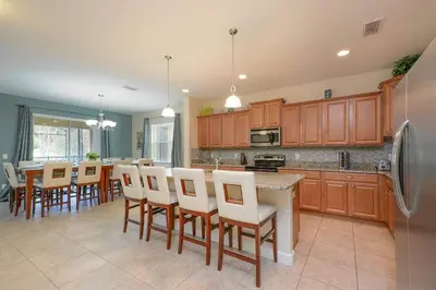 a large kitchen with wooden cabinets and white chairs at Spacious 6BR Villa Sleeps 14 in Kissimmee