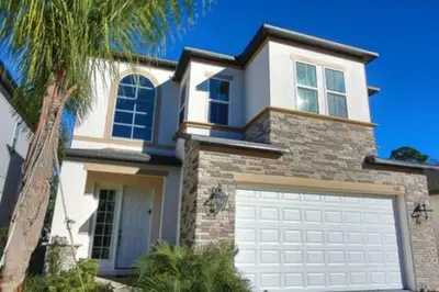 a white house with a garage door and a palm tree at Exclusive Orlando Getaway close to Disney in Kissimmee