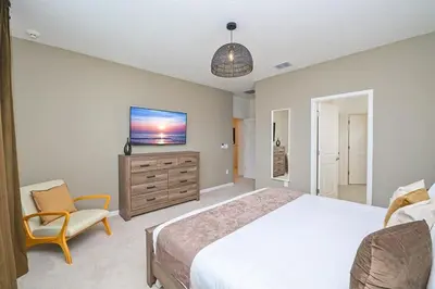 a bedroom with a bed and a tv and a chair at Brand New 12BR Disney Mansion Pool Spa Game Room in Kissimmee