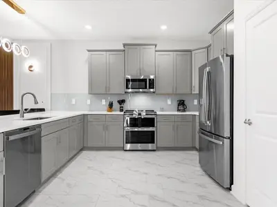 a kitchen with stainless steel appliances and white cabinets at Brand New Storey Lake 9BR Villa Summer Kitchen in Kissimmee