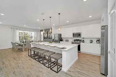 a white kitchen with a large island with bar stools at 2525 Shanti Amazing 15 Suites Mansion in Kissimmee
