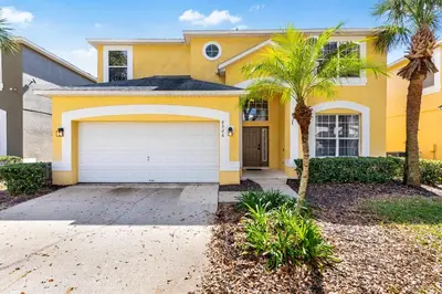 a yellow house with a garage and palm trees at Disney Doorstep 7 Bedroom Villa with SouthFacing Pool and Hot Tub in Kissimmee