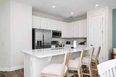 a kitchen with white cabinets and a large island with chairs at Sky Blue Villa Near Disney With Margaritaville Resort & Island H20 Waterpark Access - 3156Cs in Orlando