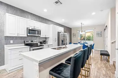 a kitchen with white cabinets and a bar with blue chairs at SUPER POSH- SLEEPs 16 wDESIGNs & NEAR Disney in Kissimmee