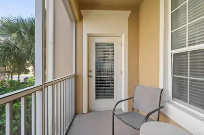 a balcony with a chair and a door with a palm tree at Cw7671-205 3Br Condo in Orlando