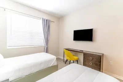 a bedroom with two beds and a tv and a yellow chair at Stylish Apartment at Vista Cay in Orlando