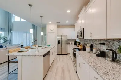 a large kitchen with white cabinets and marble counter tops at Casa Luxuosa 5Q c/ Piscina Perto da Disney! in Kissimmee