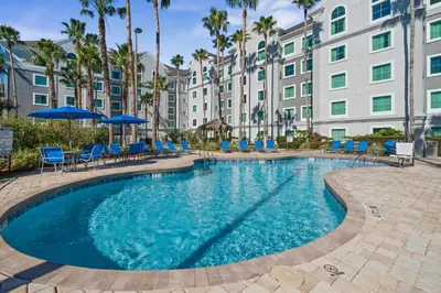 a pool with chairs and umbrellas in front of a building at Disney Potter Condo FREE Shuttle & Parking in Orlando
