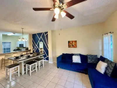 a living room with a blue couch and a kitchen at Grand Emerald 3BR Townhouse Near Disney Parks in Kissimmee