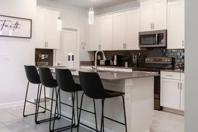 a kitchen with white cabinets and bar stools at Brand New 5 Bedrooms5Baths At Storey Lake in Kissimmee