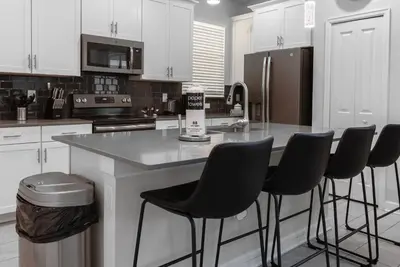 a kitchen with white cabinets and a counter with bar stools at Brand New 5 Bedrooms5Baths At Storey Lake in Kissimmee