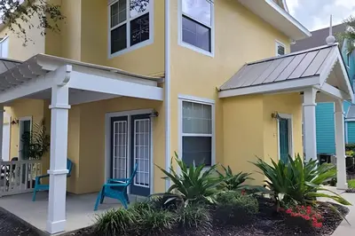 a yellow house with two blue chairs on the porch at Runaway Beach Club Condo near Disney in Kissimmee