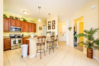 a kitchen with wooden cabinets and a island with bar stools at Tropical Lakeview Condo w. Vegas Game Room - 1014 in Orlando