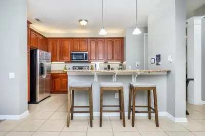 a kitchen with wooden cabinets and a island with bar stools at Stunning Vacation Condo - Vista Cay Resort - 2008 in Orlando