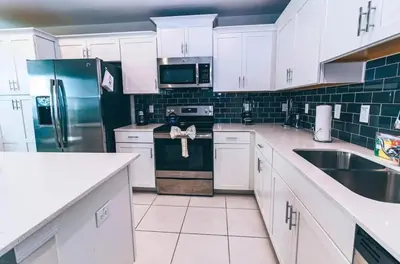 a kitchen with white cabinets and a stainless steel refrigerator at Conforto e Lazer a 7km da Disney – 2 Quartos in Kissimmee