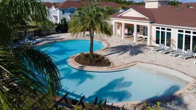 a swimming pool with a palm tree next to a house at 4BR Family Townhouse Steps to Disney in Kissimmee