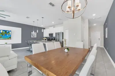 a dining room and kitchen with a wooden table and white chairs at Storey Lake Escape with Pool in Kissimmee