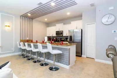 a kitchen with a bar with white chairs and a refrigerator at 4 Bedrooms3 Bathrooms at Storey Lake Resort in Kissimmee