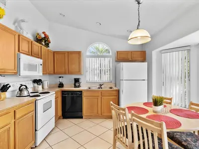 a kitchen with wooden cabinets and a table with chairs at Sunny Getaway with Private Pool, Spa & Fenced Yard in Kissimmee