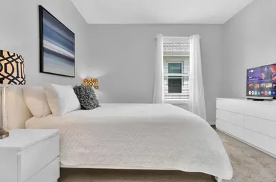 a white bedroom with a bed and a flat screen tv at 5BR Kissimmee Home Pool and Game Room Fun in Kissimmee