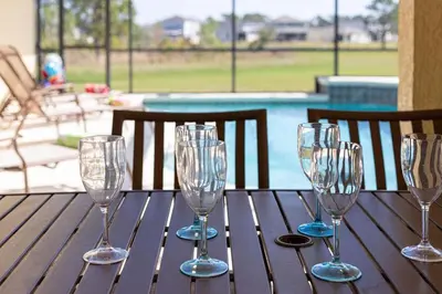 four wine glasses sitting on a wooden table near a pool at Great Location With Conservation Views in Orlando